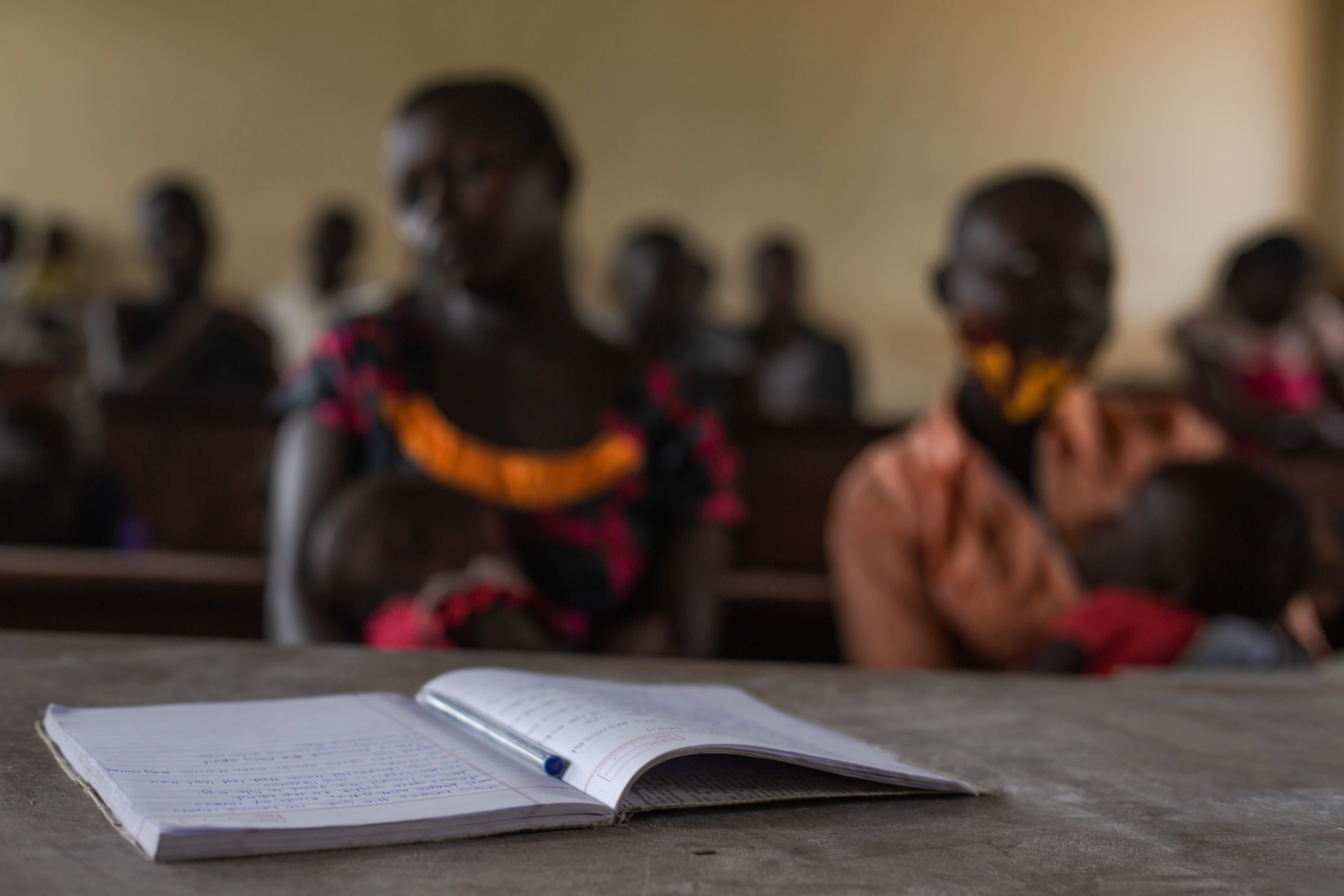 Pupils attend class at Ombaderuku Primary School, Ayivu Division, Arua District. In the background is a teenage mother attending the session with her child. The school, with a high number of teenage mothers, rising within the COVID19 lockdown has developed ways and strategies of encouraging the girls to continue with their studies.