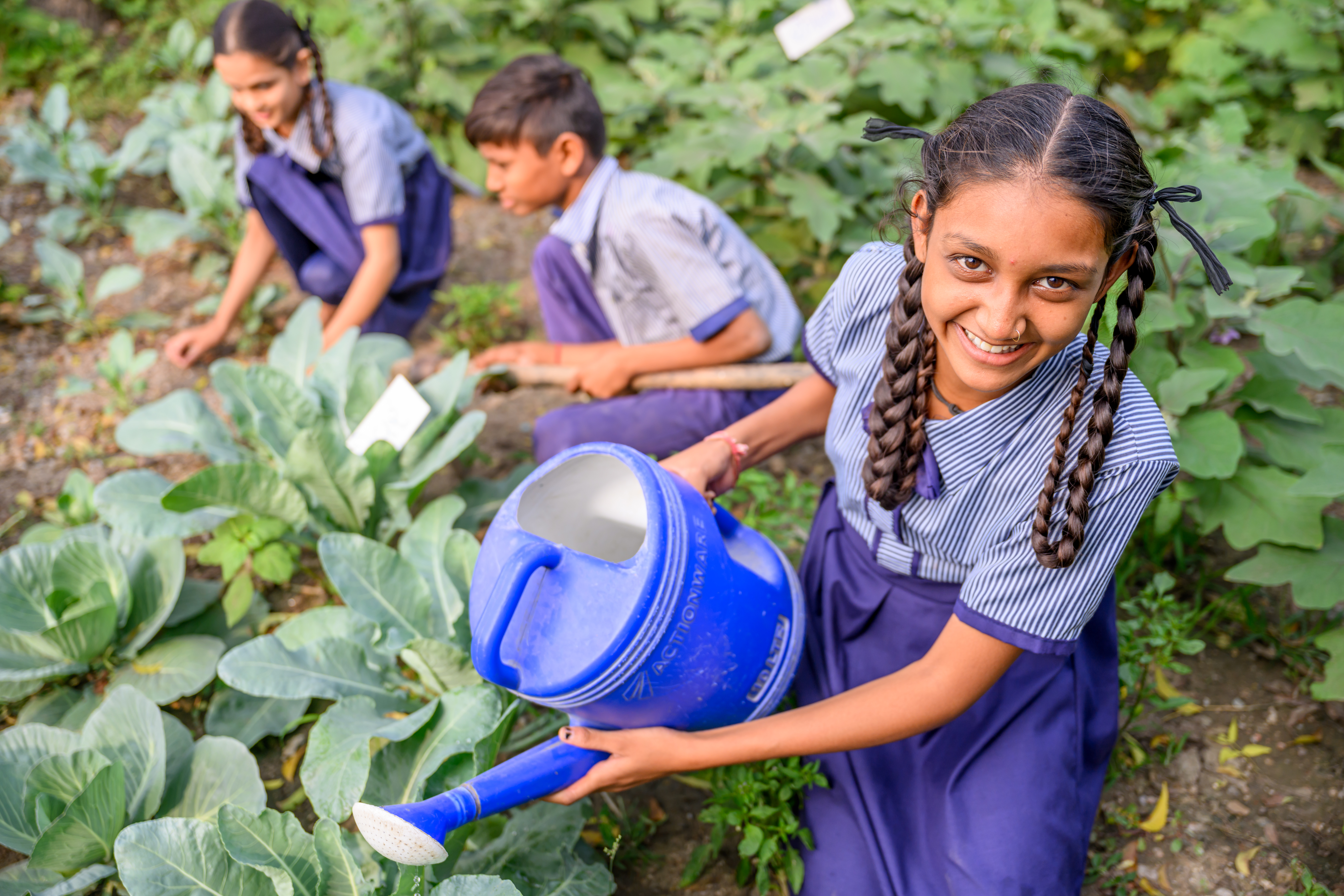 A smiling girl uses a watering can to water plants.