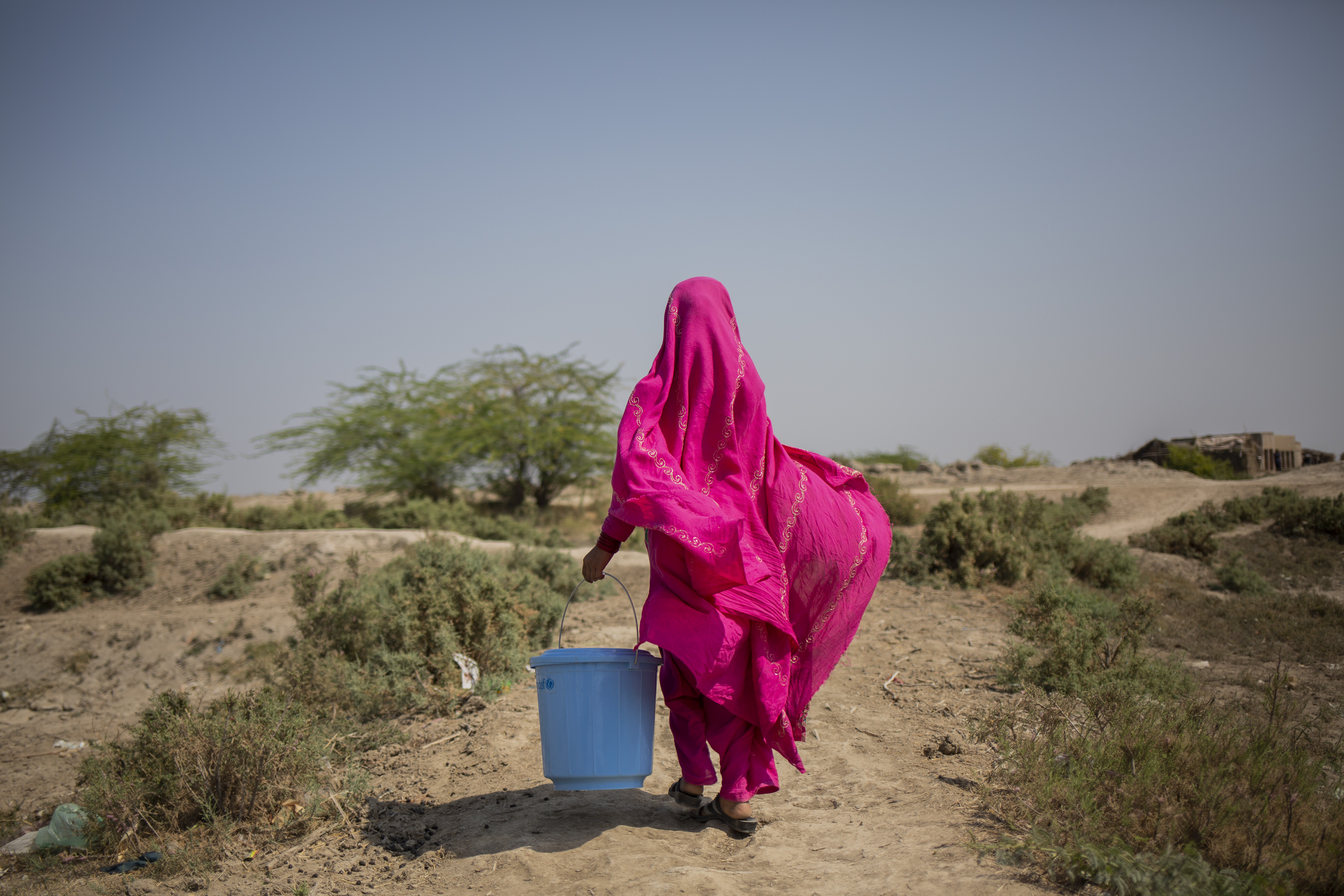 A young girl walks with a water bucket
